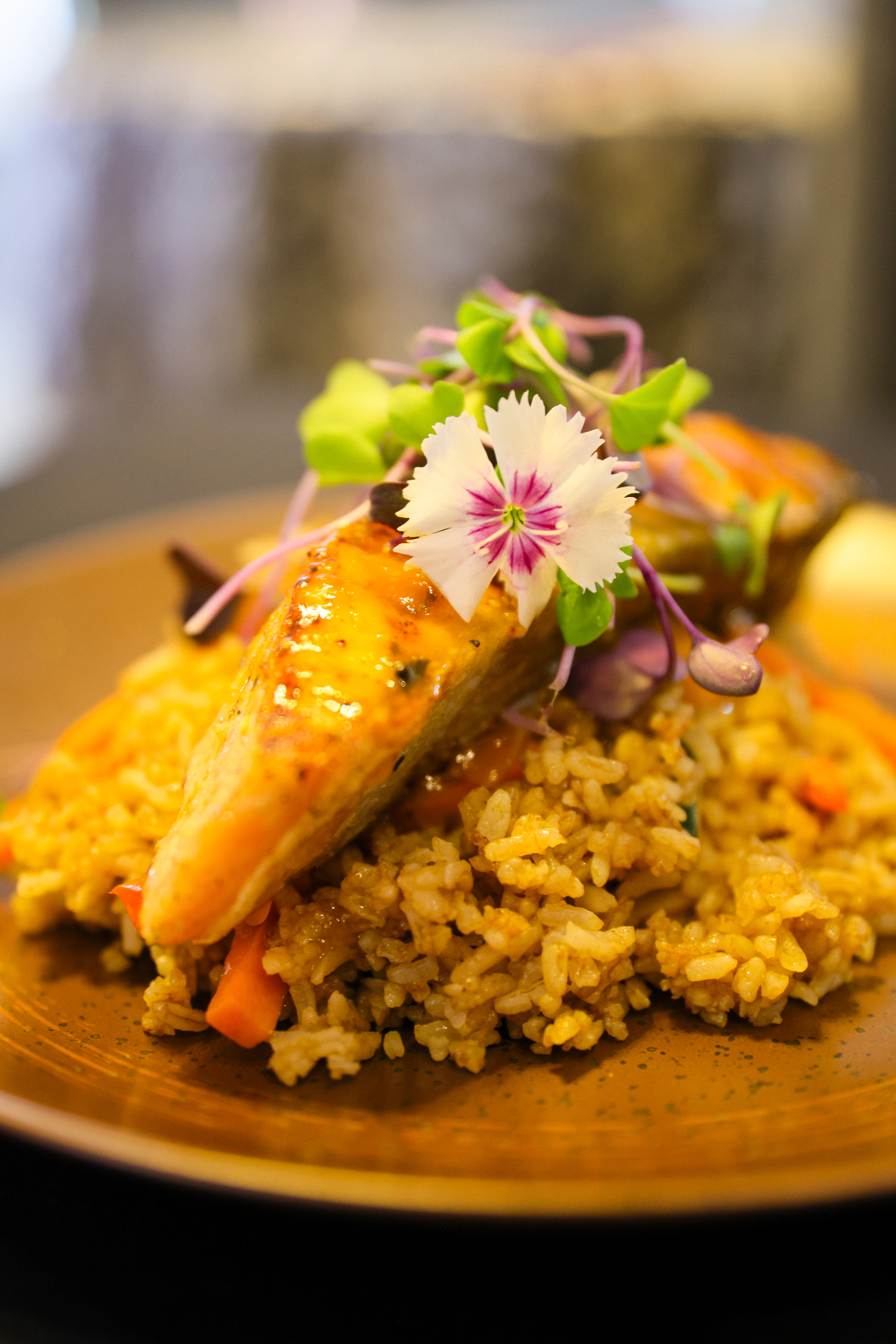 Salmón glaseado sobre arroz salteado con flores comestibles y micro vegetales